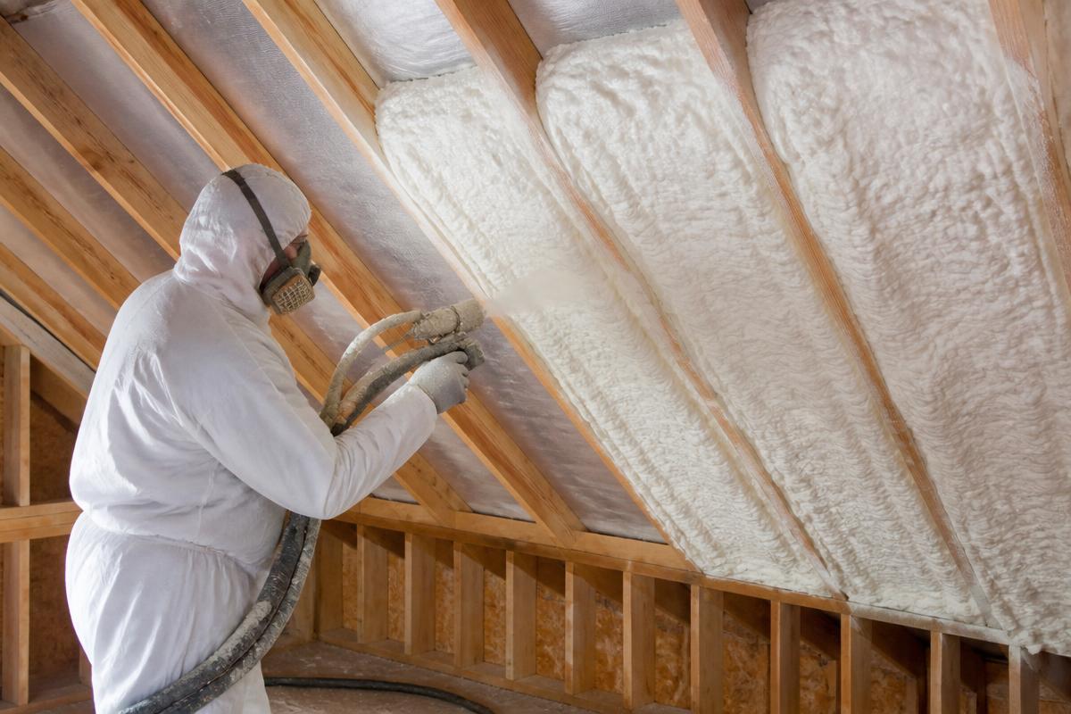 Installer spraying foam insulation between attic roof rafters